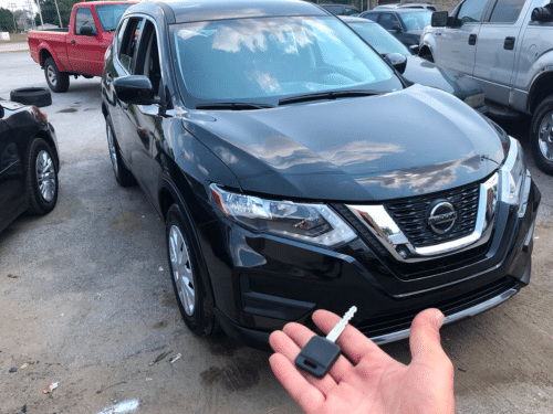 hand holding a key in front of the nissan car