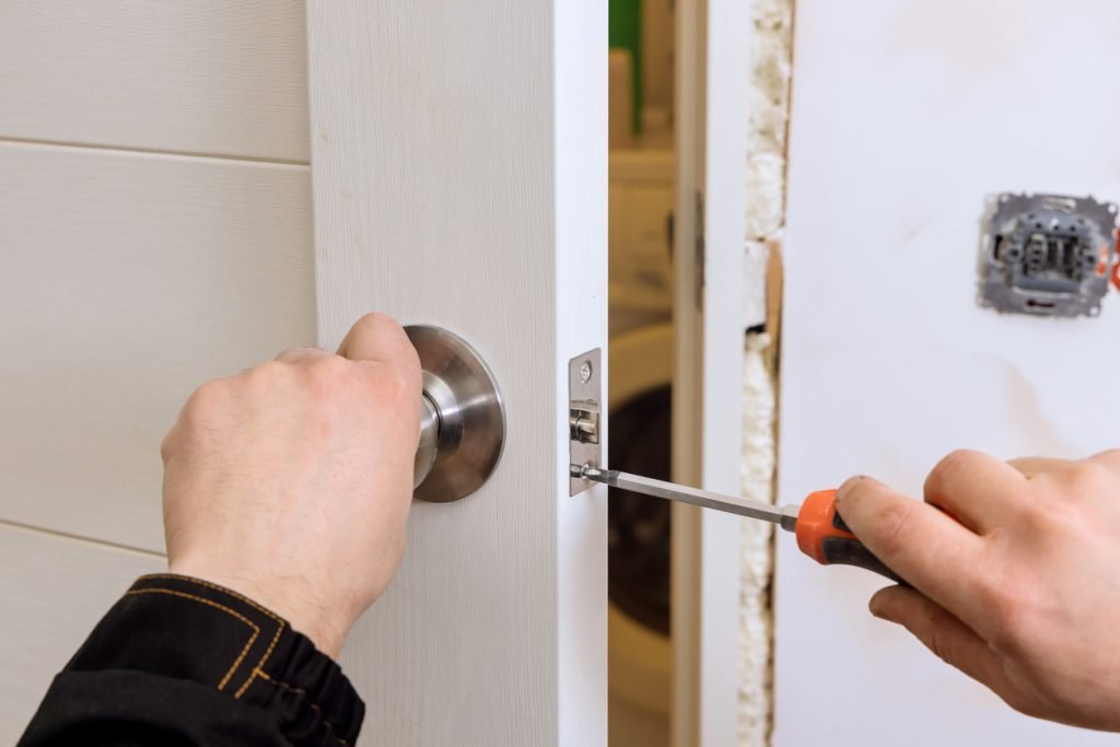 Emergency Locksmith Help for Apartment Lockouts hand holding a screw driver fixing a door knob