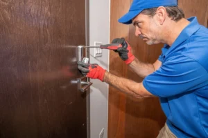 a man wearing blue cap and polo shirt holding screw driver in front of the door