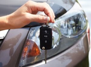 a hand holding a car key in front of the car